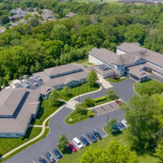 An aerial view of a large building complex surrounded by trees, with a parking lot in the foreground.