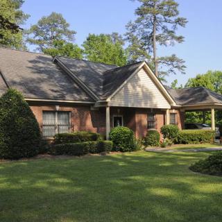 A charming brick house with a well-maintained front yard, surrounded by lush trees and bushes.