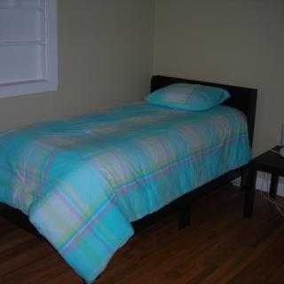 A simple bedroom with a single bed covered in a blue plaid comforter.