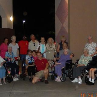 A group of people, including some in wheelchairs, gathered for a community event indoors at night.