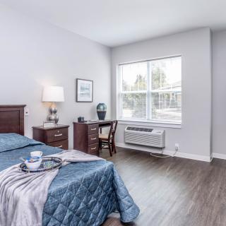 A bright and cozy bedroom with a bed, desk, and large window allowing natural light.
