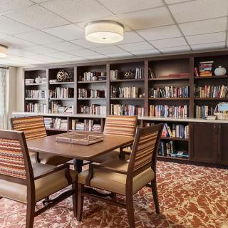 A cozy library room with a wooden table and chairs surrounded by bookshelves filled with various books.