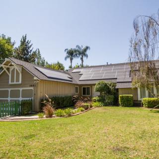 A residential house with solar panels on the roof and a spacious front yard.