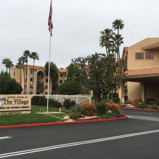 Entrance to a resort with palm trees and a sign displaying 'The Village'.