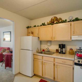 A compact kitchen with light wooden cabinets, a refrigerator, and a stove, adjoining a dining area.