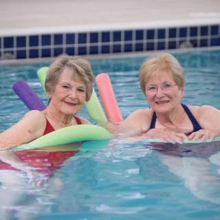 Two women enjoying a swim with pool noodles.