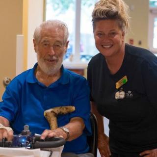 An elderly man in a wheelchair smiling with a caregiver beside him.