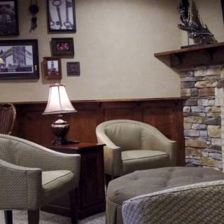A cozy living room with comfortable chairs around a stone fireplace, adorned with warm lighting and decor.