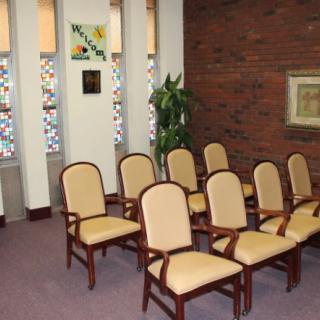 A neatly arranged small room with rows of chairs, stained glass windows, and decorative elements.