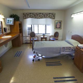 A clean and organized hospital room with a single bed and functional furniture.