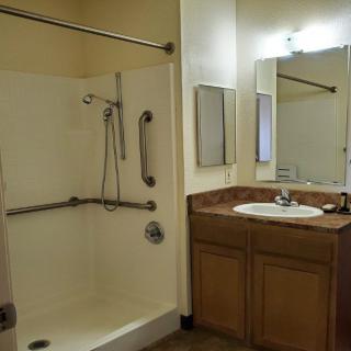 An accessible bathroom featuring a shower with handrails and a sink with a mirror above it.