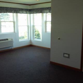 A bright, empty room with carpeted flooring and large windows letting in natural light.