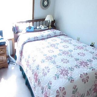 A cozy bedroom with a floral quilt on the bed and a nightstand with a lamp by the window.