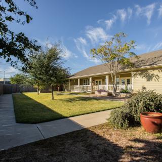 A well-maintained lawn with trees and a pathway leading to a house under a clear blue sky.