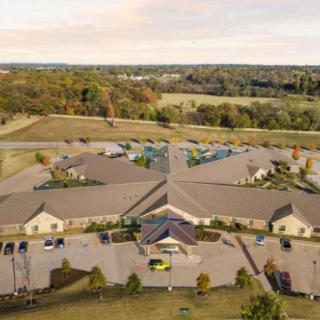 Aerial view of a large building complex with surrounding greenery and parking areas.