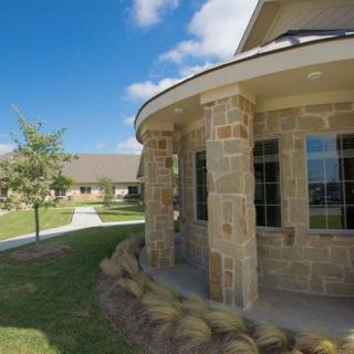 A stone building surrounded by a landscaped lawn and pathways under a clear blue sky.