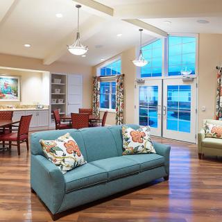 A modern and cozy living room with a blue sofa, wood flooring, and a connected dining area.