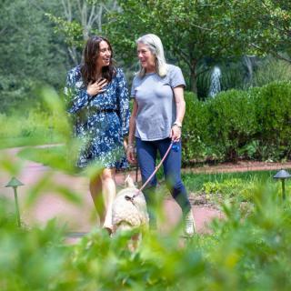 Two women walking a dog in a garden setting.