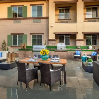 A cozy outdoor patio with a dining area featuring wicker chairs, a wooden table adorned with sunflowers, and a building backdrop.