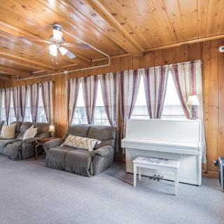 A cozy living room featuring wood paneling, comfortable sofas, and a piano, bathed in natural light.