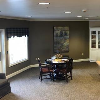 A cozy living room with a table and chairs, featuring a large window and wall art.