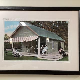 A vintage photograph of a family gathered on the porch of their house, surrounded by nature.
