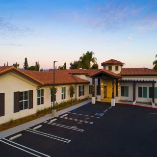 A modern building with a parking lot in front, set against a sunset sky.