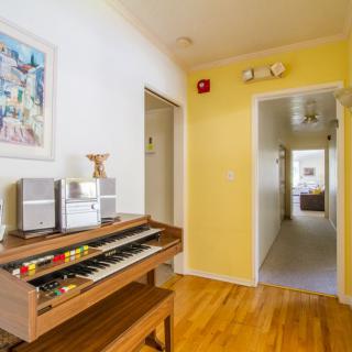 A bright hallway featuring a wooden piano on a hardwood floor, adorned with artwork and vibrant decor.
