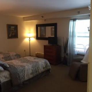 A cozy bedroom with a bed, dresser, mirror, and a lamp near the window.