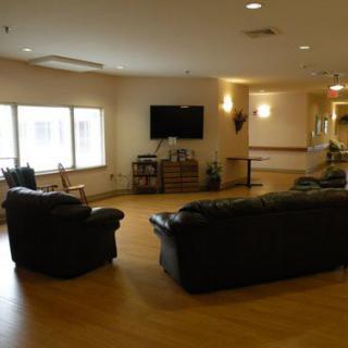 A cozy living room with couches, armchairs, and a TV on the wall.