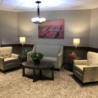 A cozy living room with a sofa, two chairs, and a coffee table, all warmly lit by stylish lamps and decorated with artwork on the wall.