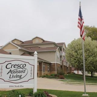An assisted living facility with a sign out front and an American flag in the background.