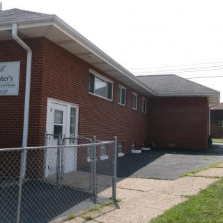A brick church building with a chain-link fence and a small parking area.