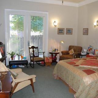 A cozy bedroom with warm decor and comfortable furniture, featuring a bed, armchair, and a window with blinds.