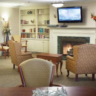 A cozy living room with armchairs facing a fireplace and television, surrounded by bookshelves.