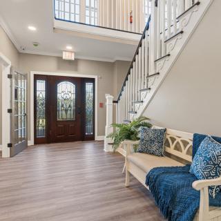 A welcoming foyer with a staircase, wooden flooring, and a decorative bench under natural lighting.
