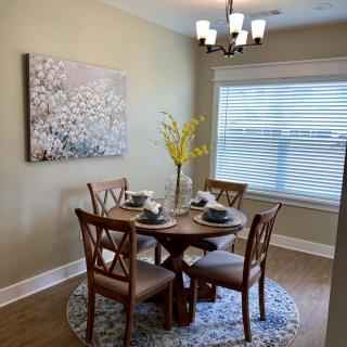 A cozy dining room with a round wooden table set for four, adorned by modern decor and wall art.