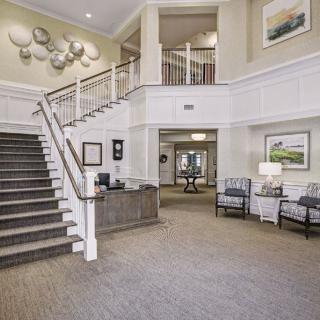 A spacious and elegantly decorated lobby featuring a staircase, seating area, and artwork on the walls.