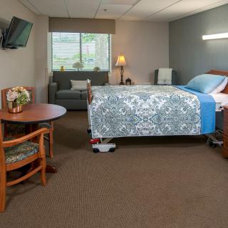 A clean and well-furnished hospital room with a bed, armchair, table, and television.