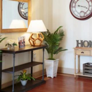 A cozy living room corner featuring a decorative table with plants, a lamp, and a wall-mounted mirror and clock.