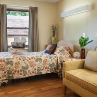 A cozy bedroom with floral bedding and a comfortable armchair, featuring warm colors and natural light.