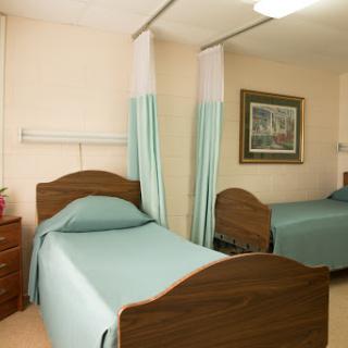 A view of a shared patient room in a hospital, featuring two beds with green bedspreads and curtains for privacy.