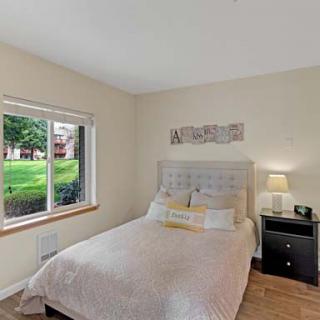 A cozy bedroom with a neatly made bed, a nightstand with a lamp, and a window providing natural light.