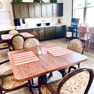 A cozy dining area with neatly arranged tables and chairs, featuring a kitchen in the background.