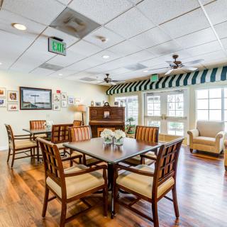 A cozy dining area with wooden tables and chairs, framed by large windows and soft lighting.