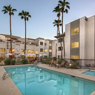 A modern apartment complex with a swimming pool and palm trees in the evening.