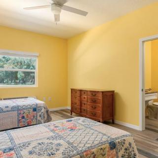A cozy bedroom with yellow walls, featuring two beds, a wooden dresser, and a ceiling fan.