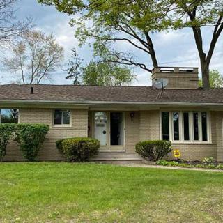 A suburban ranch-style single-story house with a well-maintained lawn and surrounding trees.