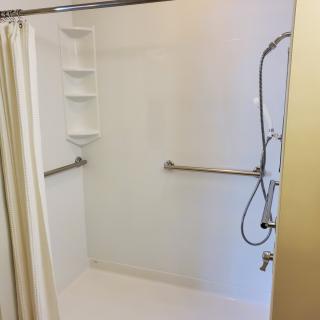 An accessible bathroom shower with grab bars and a wall-mounted showerhead.