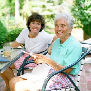 An elderly woman and a younger woman sitting together outdoors, enjoying a sunny day in the garden.
